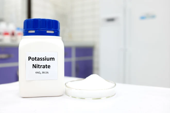 Selective focus of a bottle of pure potassium nitrate chemical compound beside a petri dish with solid crystalline powder substance